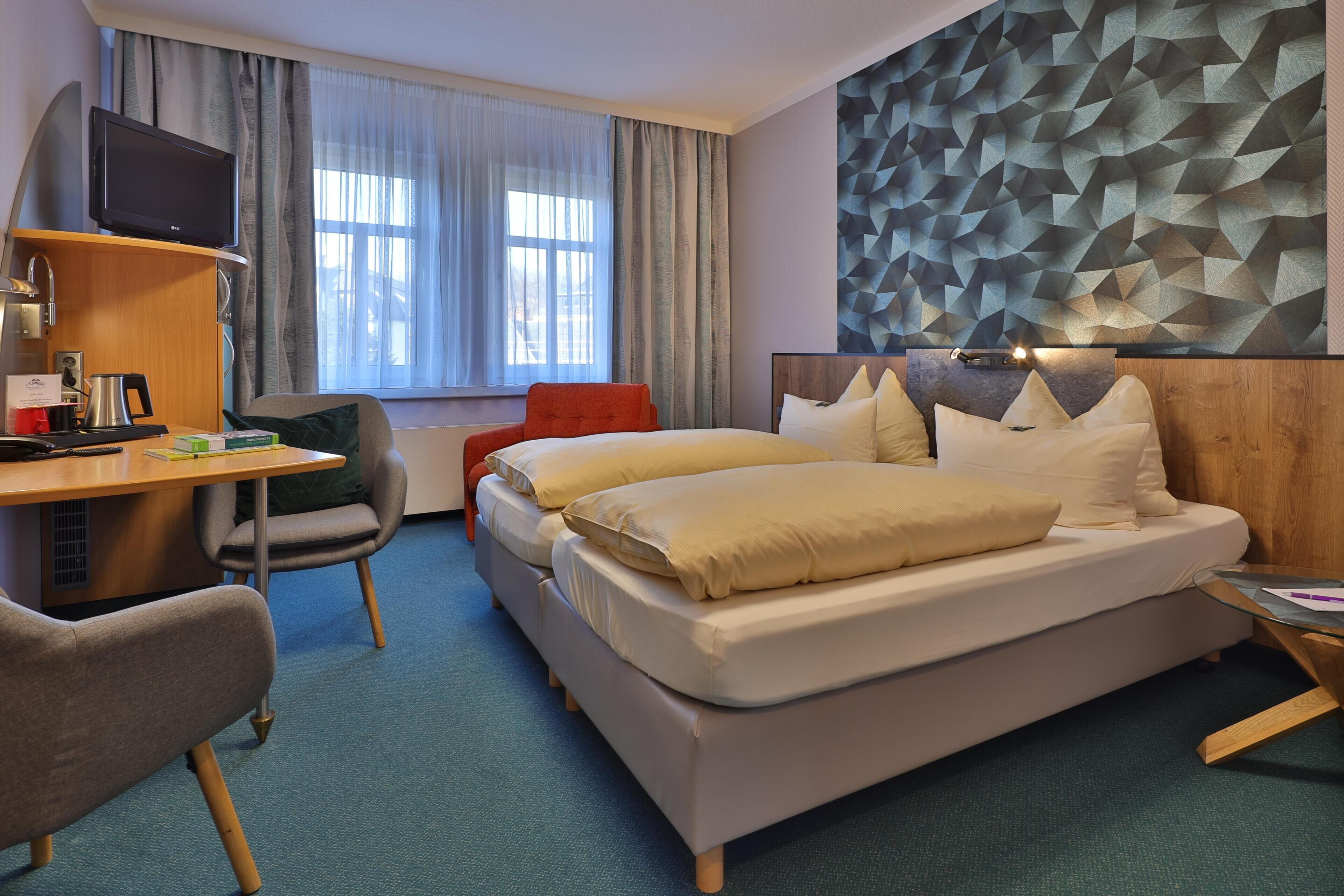 Een hotelkamer met een bed, een bureau met een computer, een stoel en een televisie.