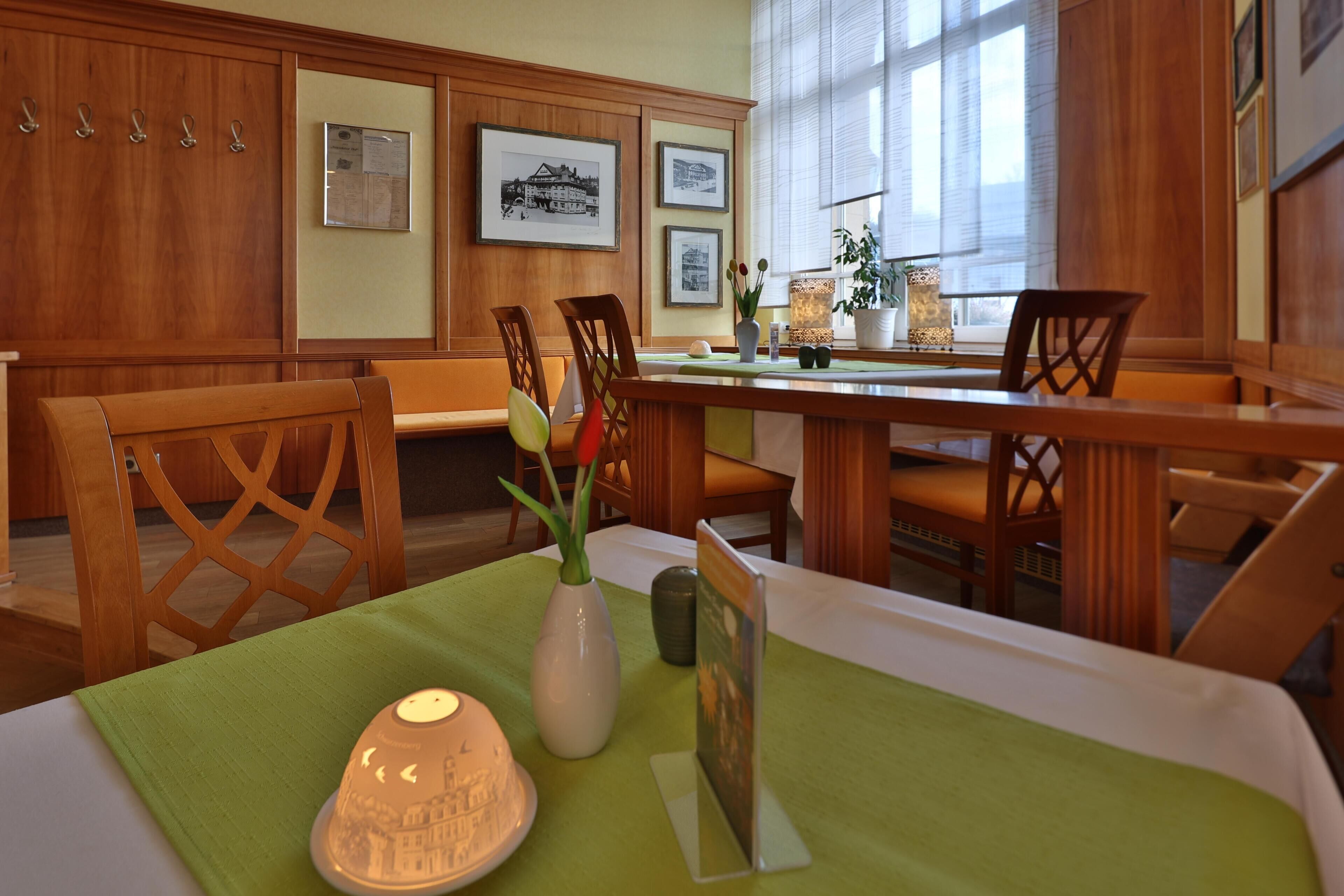 Un comedor con muebles de madera, mantel verde, un florero con flores y cuadros en la pared.