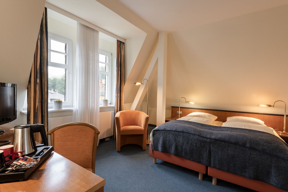 A hotel room with a bed, a desk with a coffee maker, a chair, and a TV.