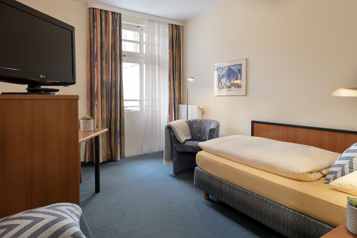 A hotel room with a bed, a TV, a chair, a lamp, and a painting on the wall.