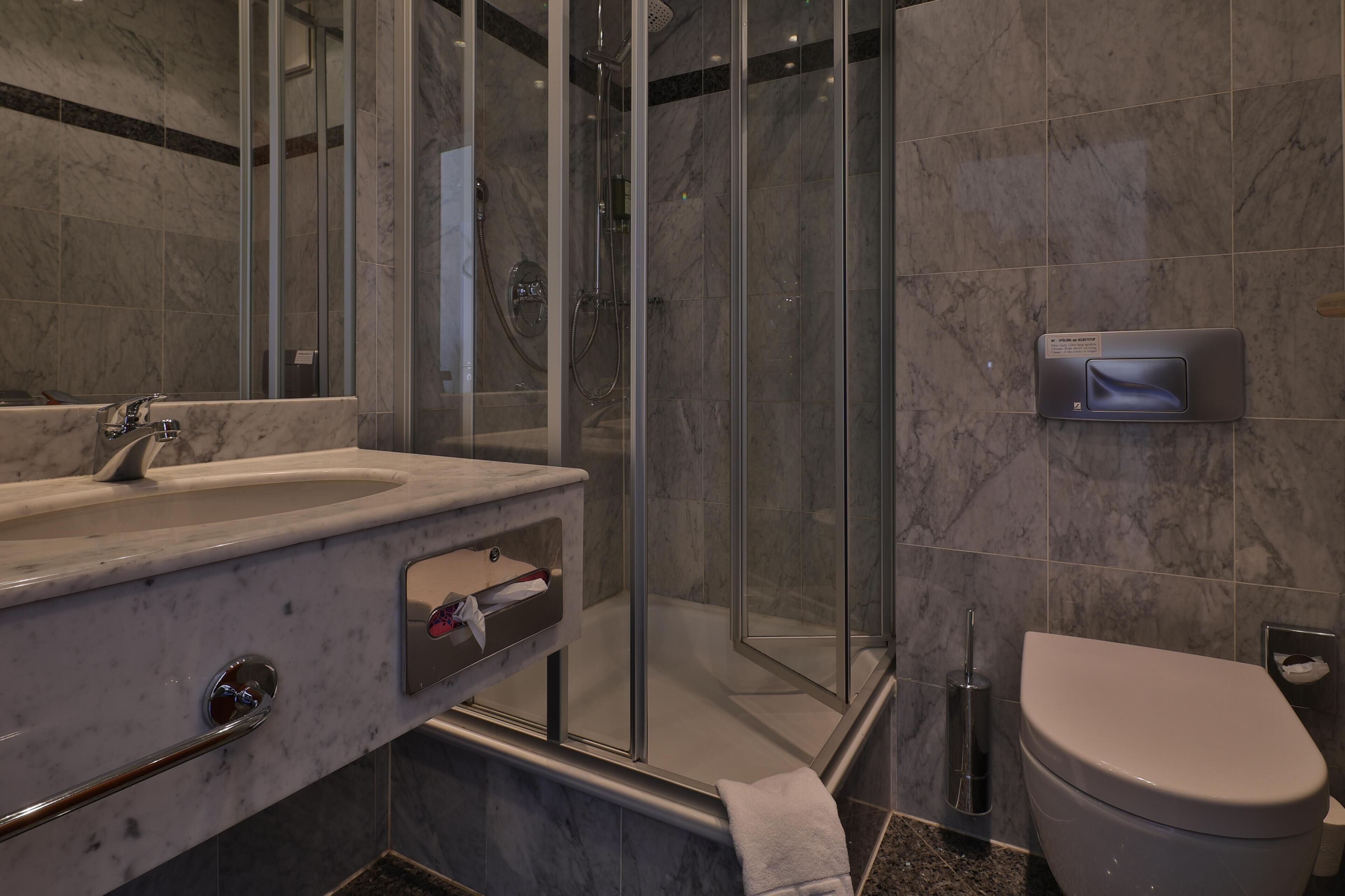 Ein modernes Badezimmer mit Marmorwaschbecken, einer Duschkabine aus Glas und einer Toilette.