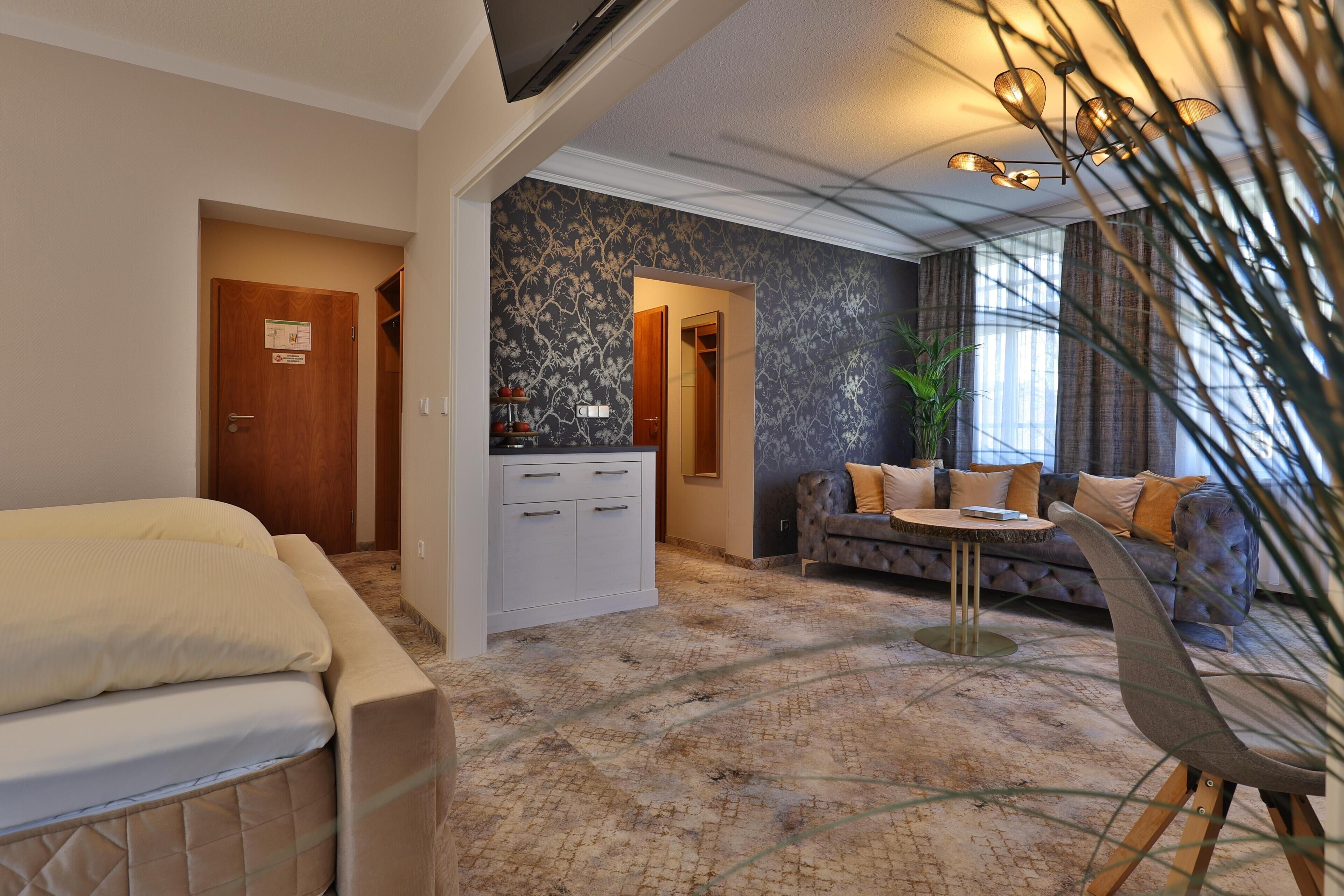 A hotel room with a bed, a sofa, a small table, a cabinet, and a large window with curtains.