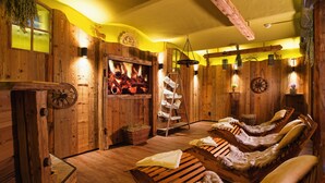 Une salle de spa en bois, dotée d’une cheminée, de bancs en bois et de plantes suspendues.