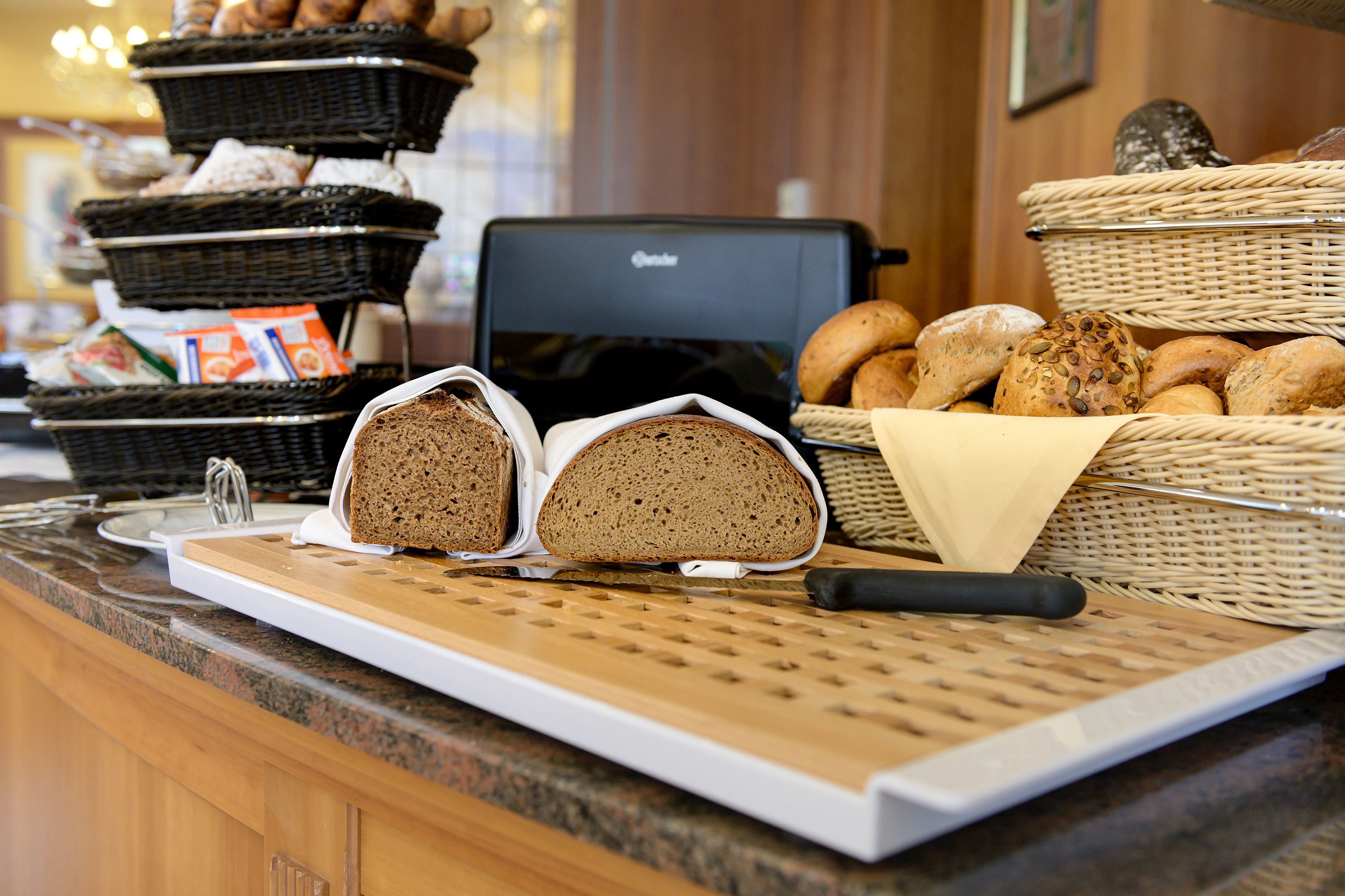 A bakery display with various breads and pastries, a bread slicer, and baskets of bread.