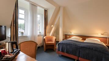 Ein Hotelzimmer mit Bett, Schreibtisch mit Kaffeemaschine, Sessel und Fernseher.