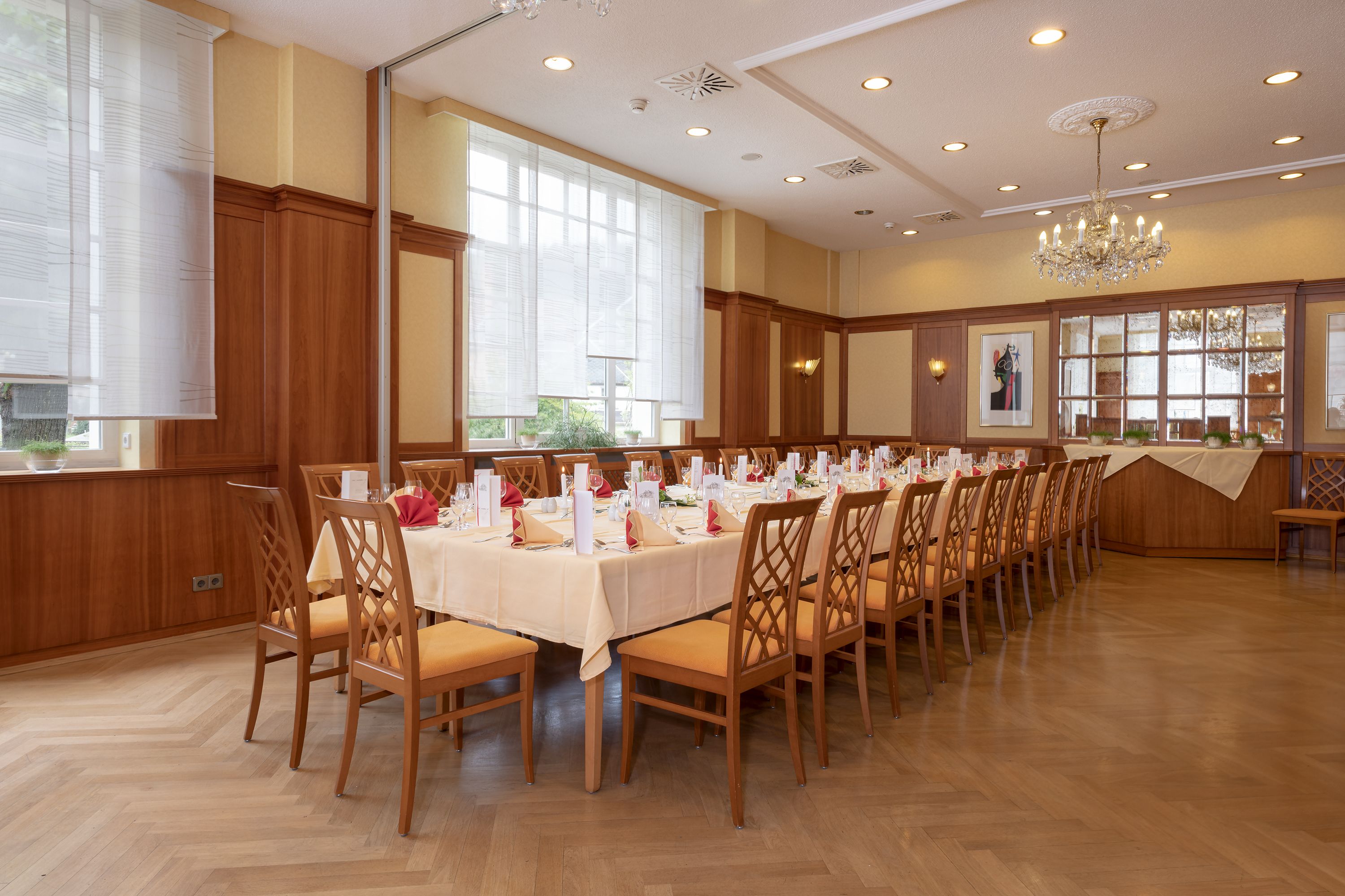 Une grande salle de banquet avec de longues tables dressées pour un événement formel, des boiseries et un lustre.