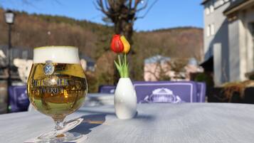 Una cerveza en una mesa, con una tulipa y un jarrón blanco al fondo.