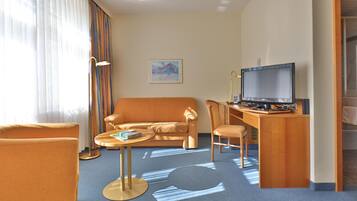 Habitación de hotel con sofá, escritorio con computadora, lámpara y un cuadro en la pared.