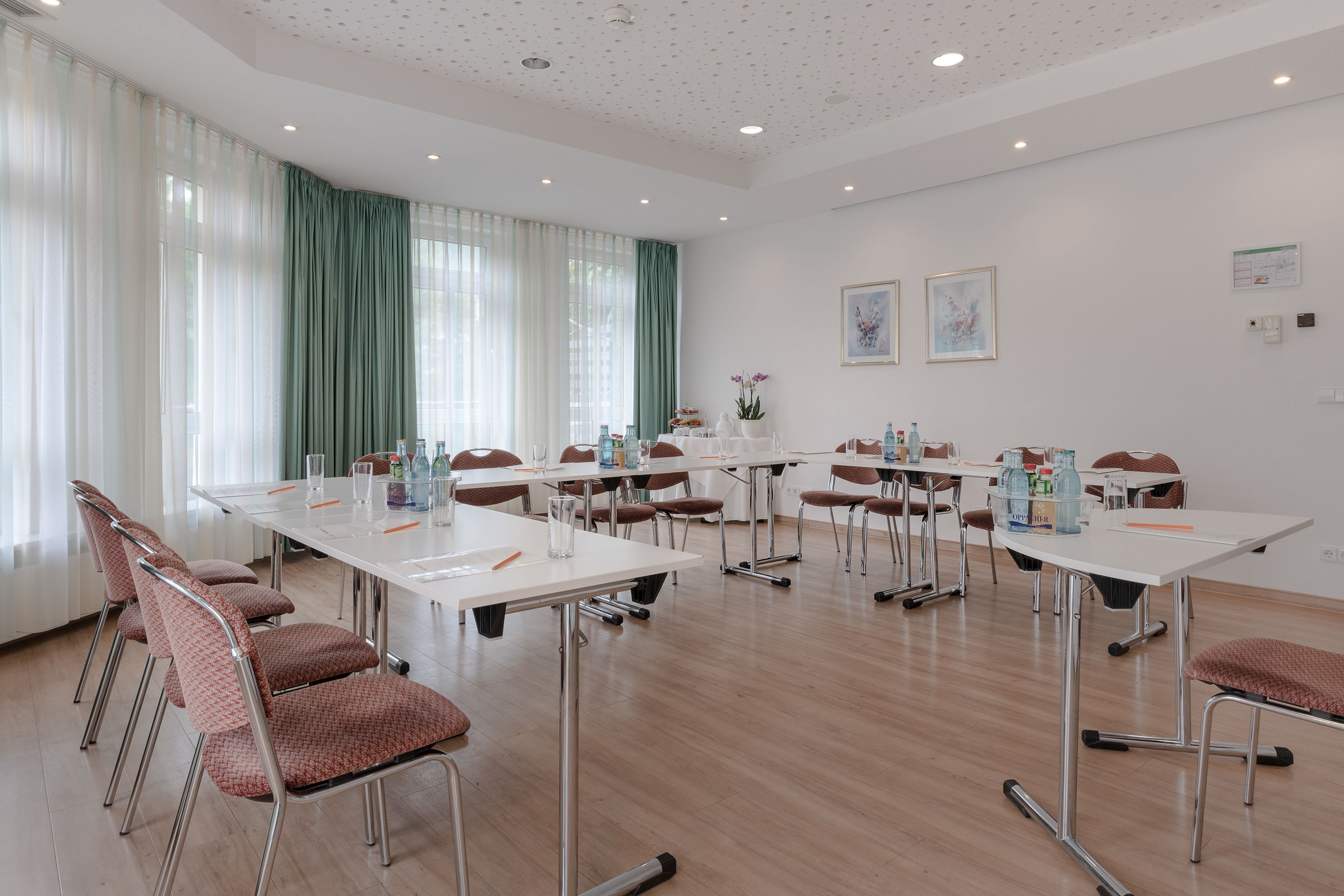 A conference room with white tables, brown chairs, and a large window with green curtains.