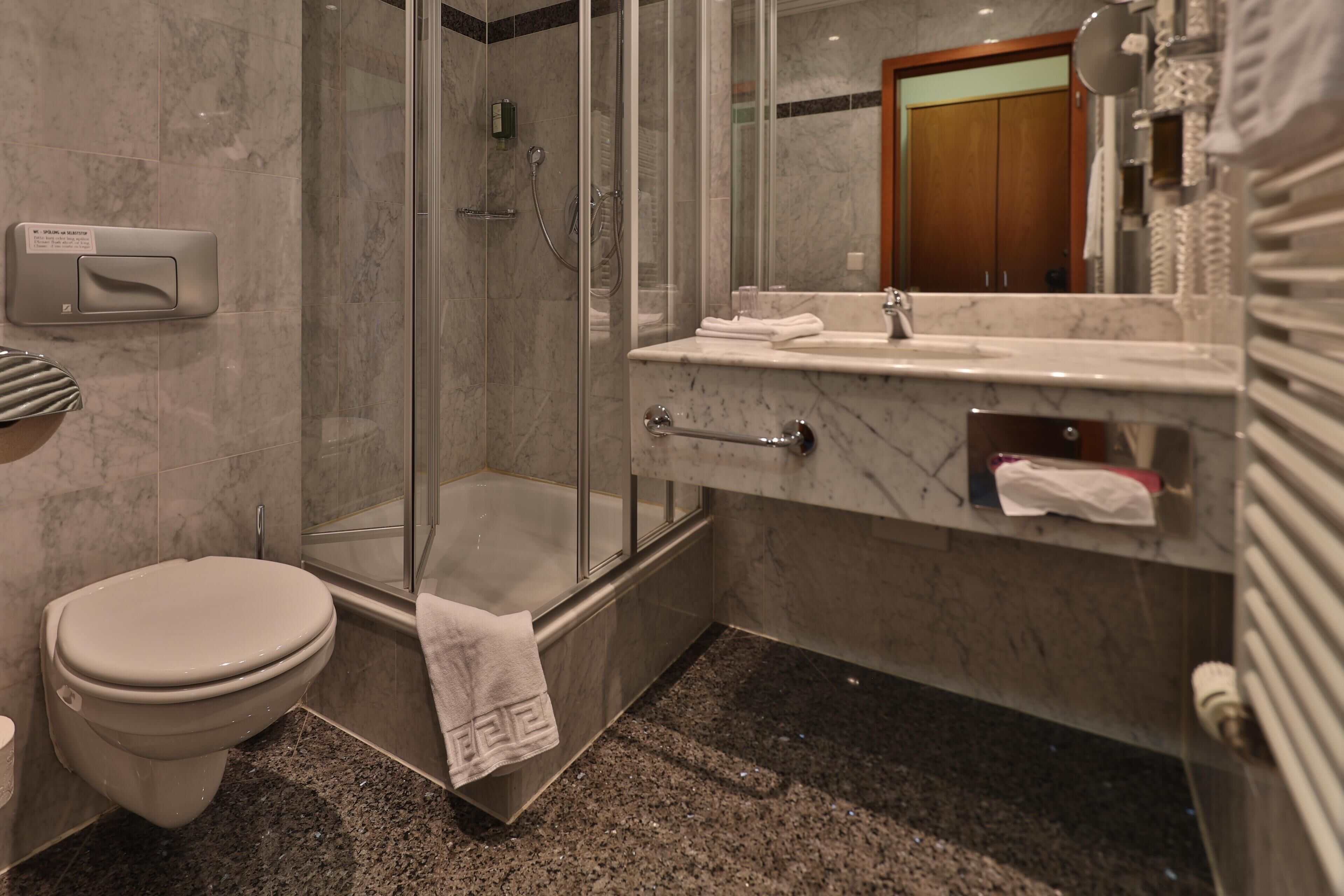 A modern bathroom with a glass-enclosed shower, a marble sink, and a toilet.