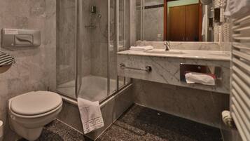 A modern bathroom with a glass-enclosed shower, a marble sink, and a toilet.