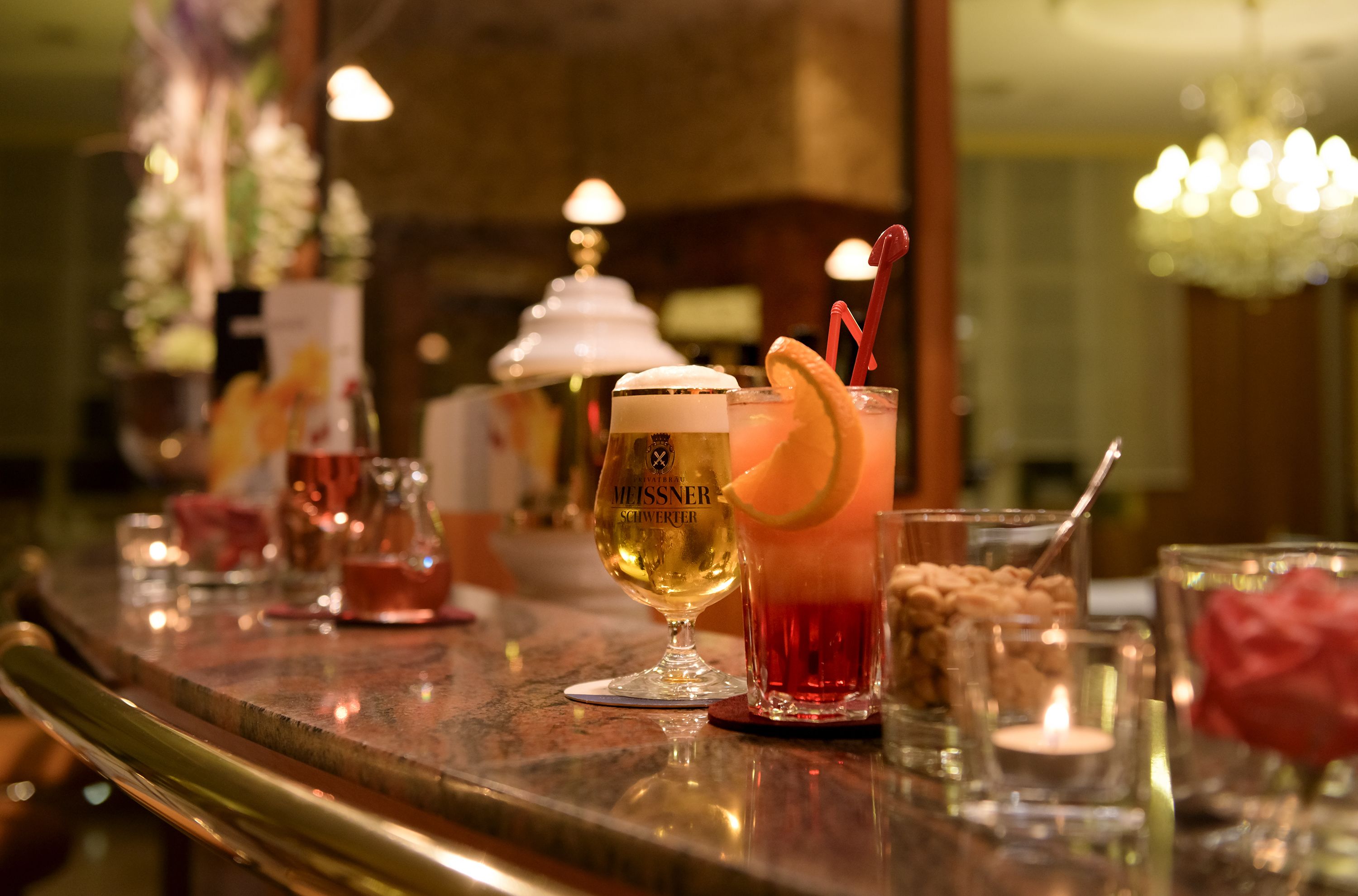 A bar area with various drinks and glasses, including a tall glass with a lemon garnish and a smaller glass with a red drink and a straw.