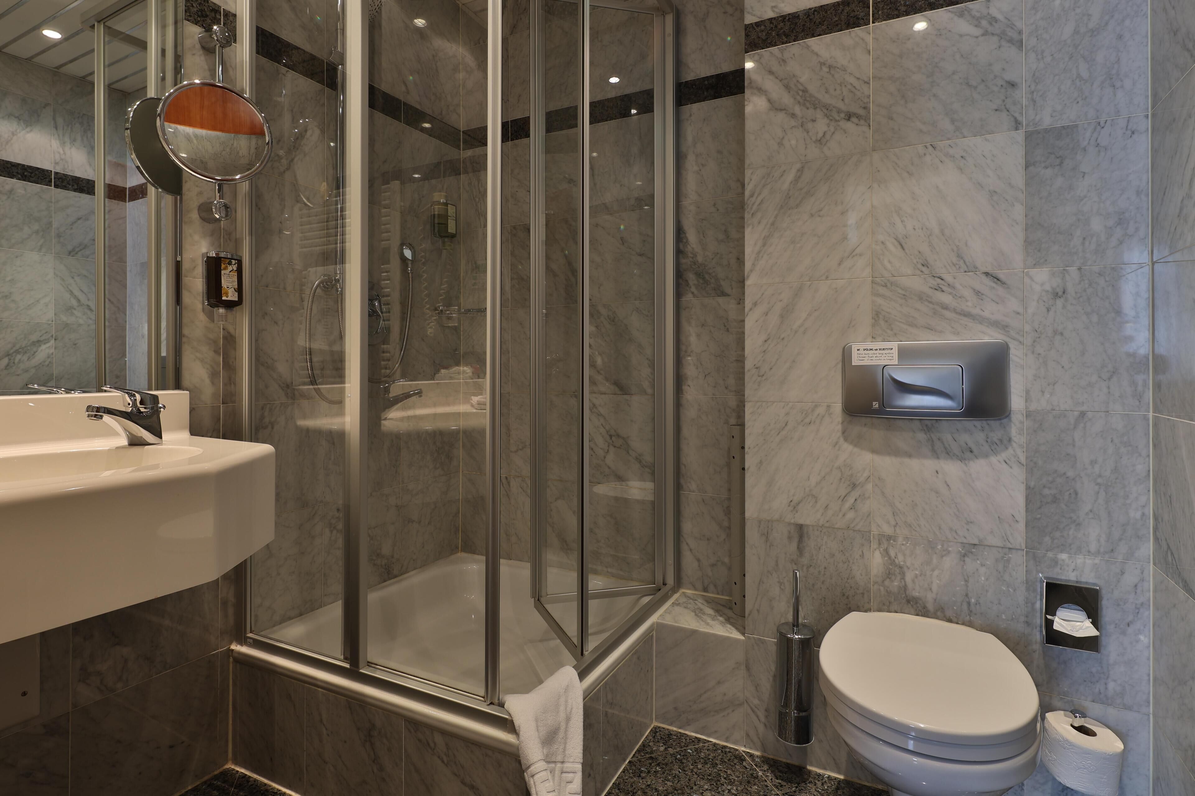 A modern bathroom with a glass-enclosed shower, a white sink, and a toilet.