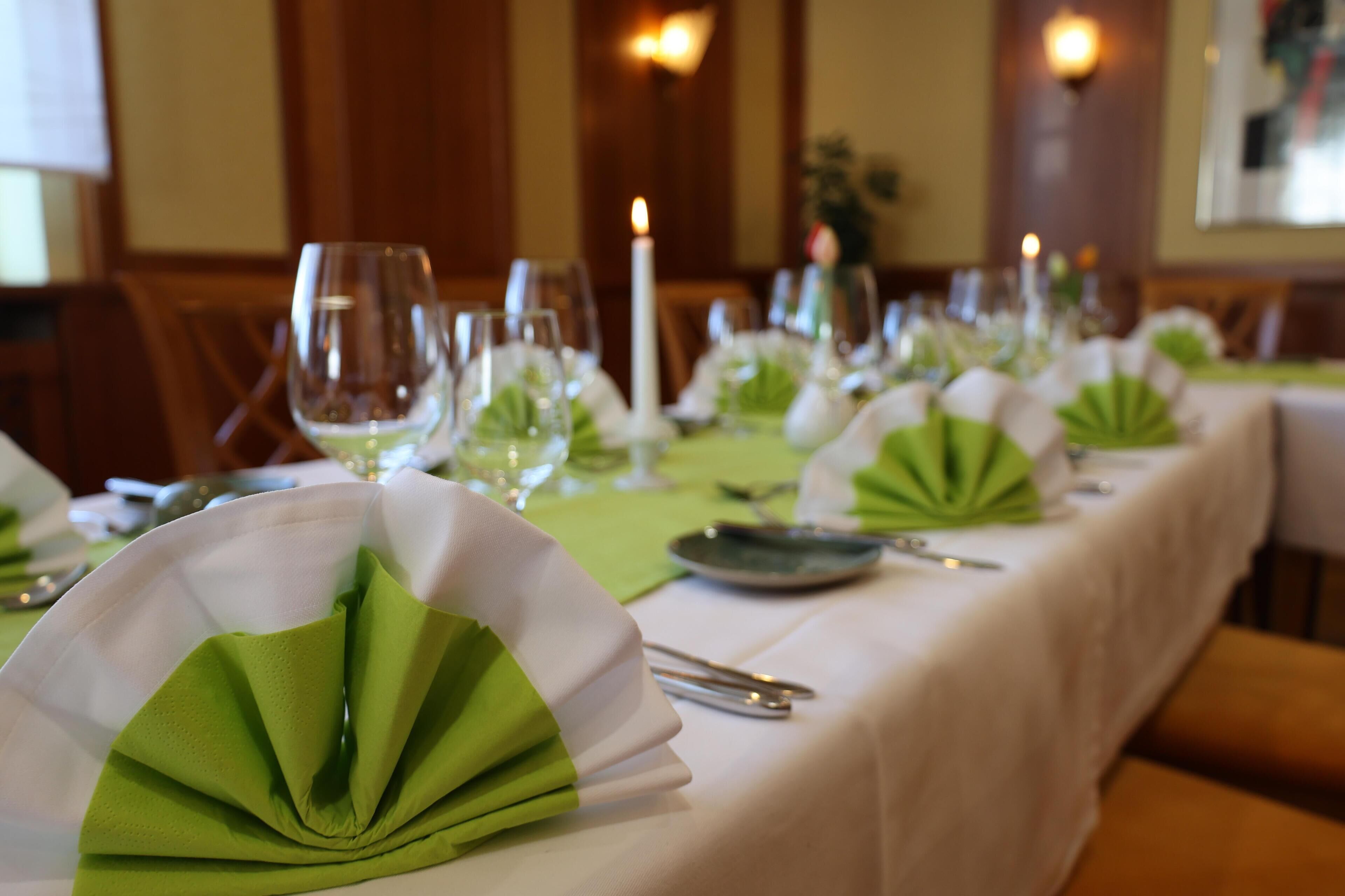 Une table à manger dressée avec des serviettes vertes et blanches, une nappe blanche et des bougies.