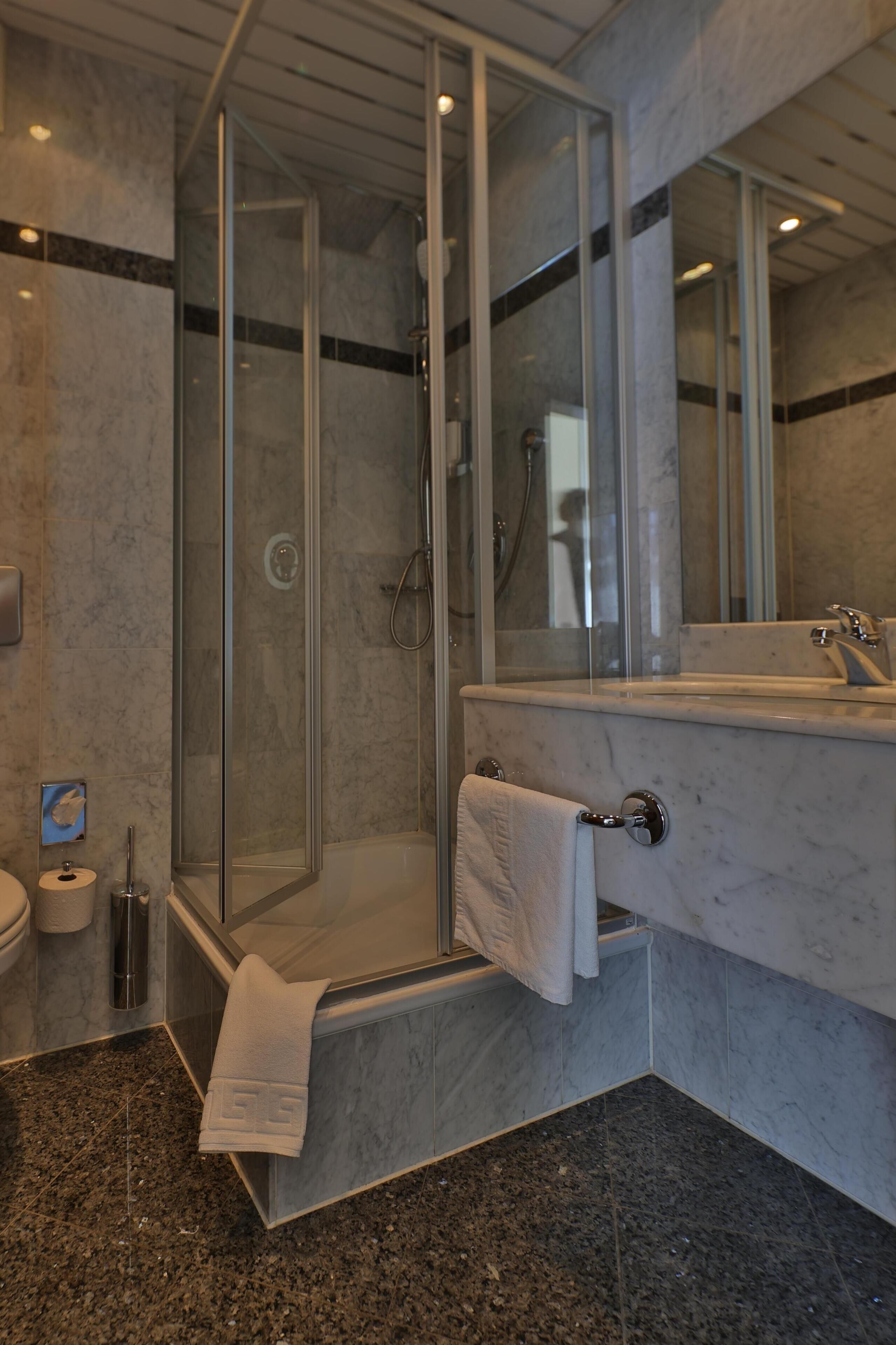 A modern bathroom with a glass-enclosed shower, a marble sink, and a towel rack.