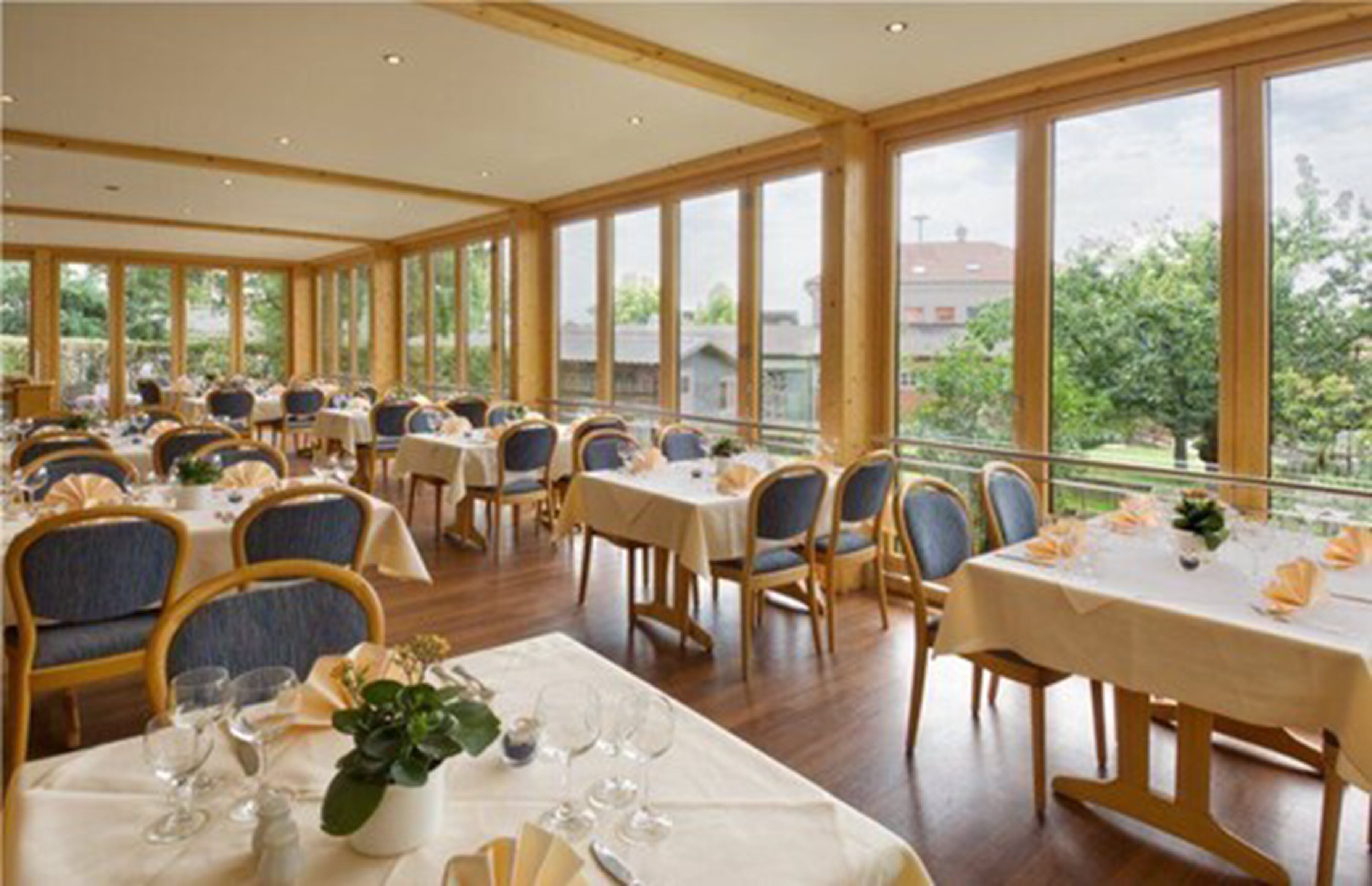 Ein Restaurant mit mehreren Tischen und Stühlen, großen Fenstern und Blick ins Freie.