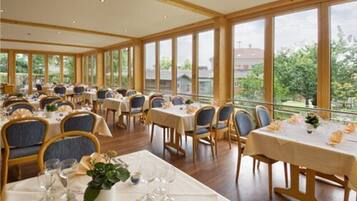 Ein Restaurant mit mehreren Tischen und Stühlen, großen Fenstern und Blick ins Freie.