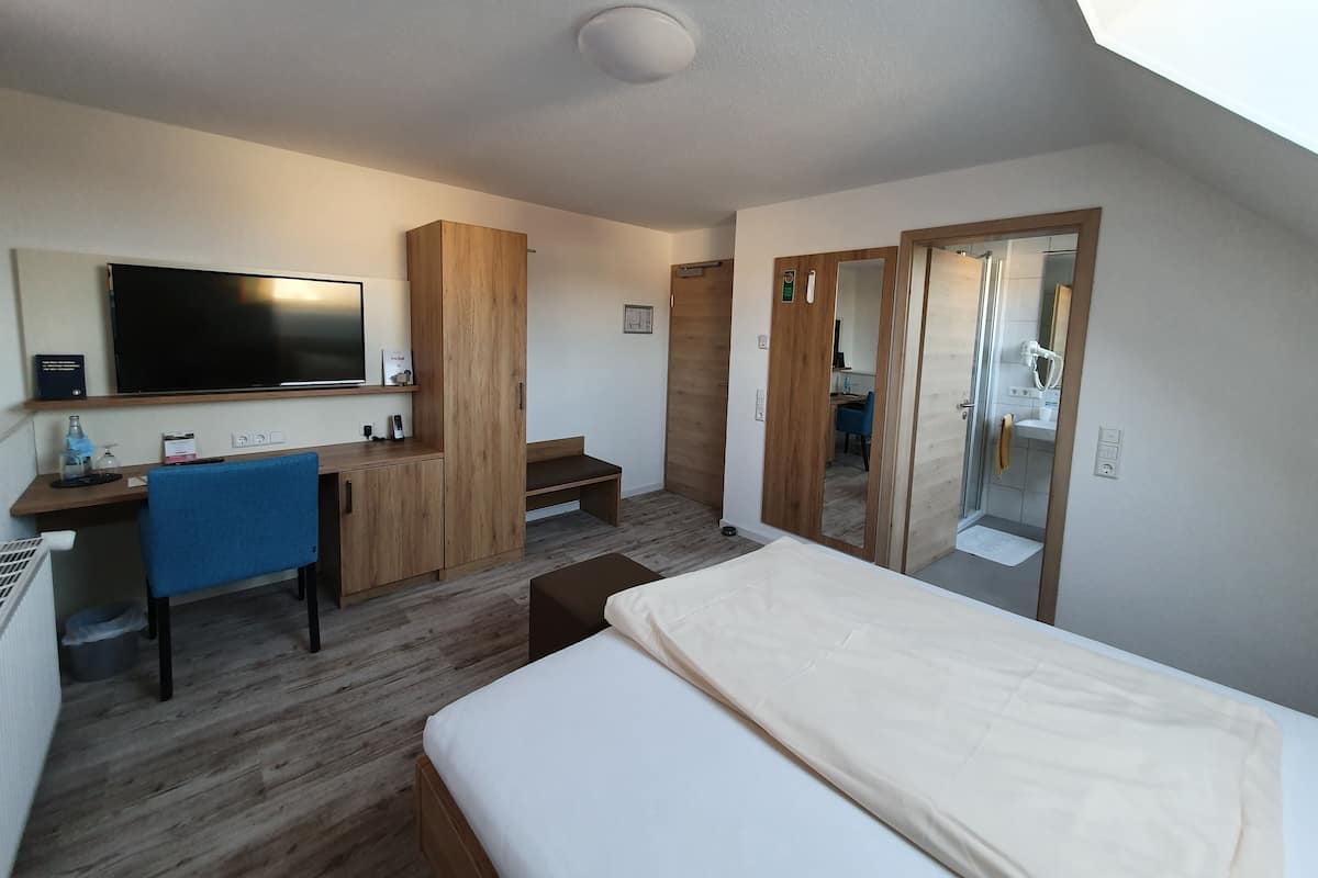 Una habitación de hotel moderna con una cama grande, un escritorio con una silla, un televisor y un espejo.