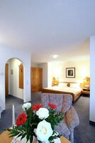 Quarto de hotel com cama, uma cadeira, uma mesa com um vaso de flores e um quadro pendurado na parede.