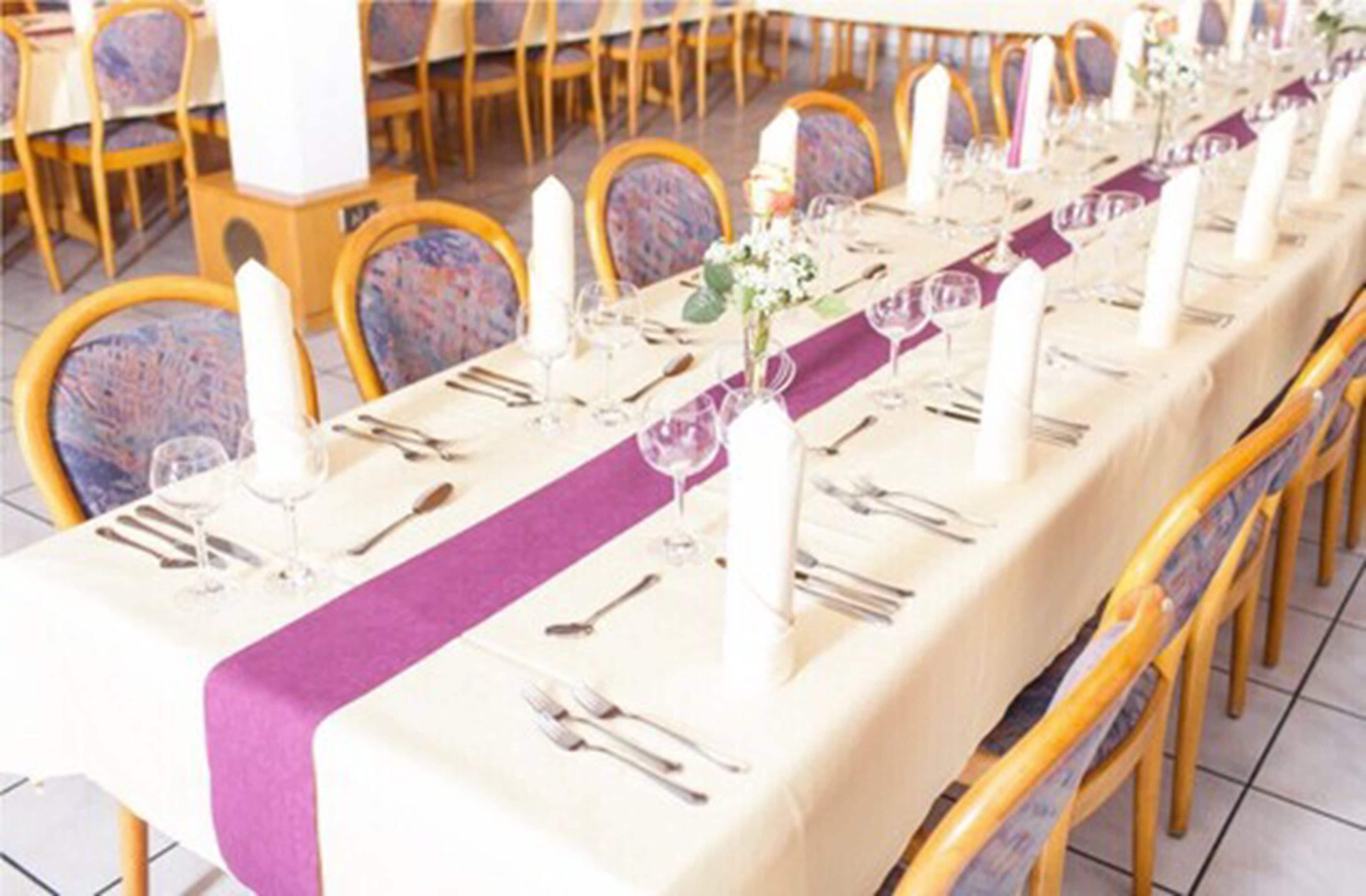 Una larga mesa de comedor cubierta con manteles blancos, caminos de mesa morados y velas blancas.