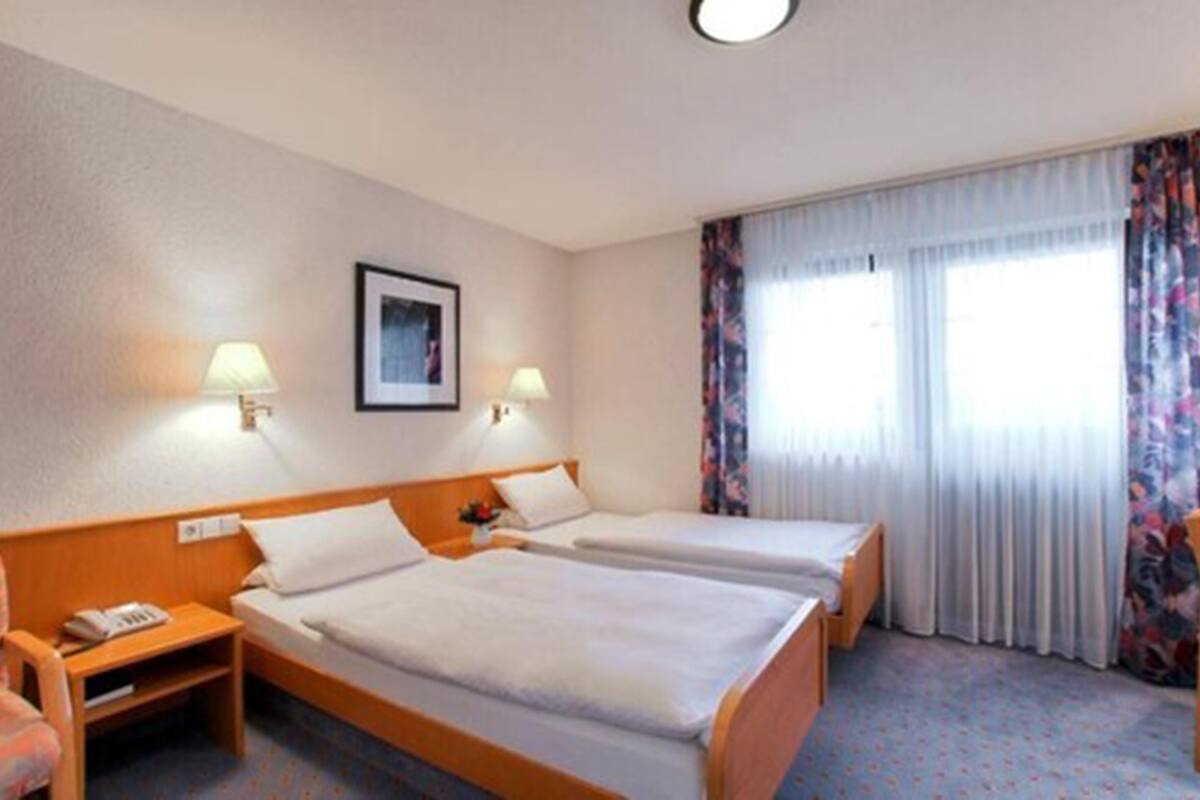 Una habitación de hotel con dos camas, una mesita de noche, una silla y una ventana con cortinas.