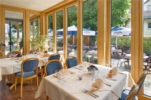 Restaurante com mesas montadas para refeições, grandes janelas e área externa.