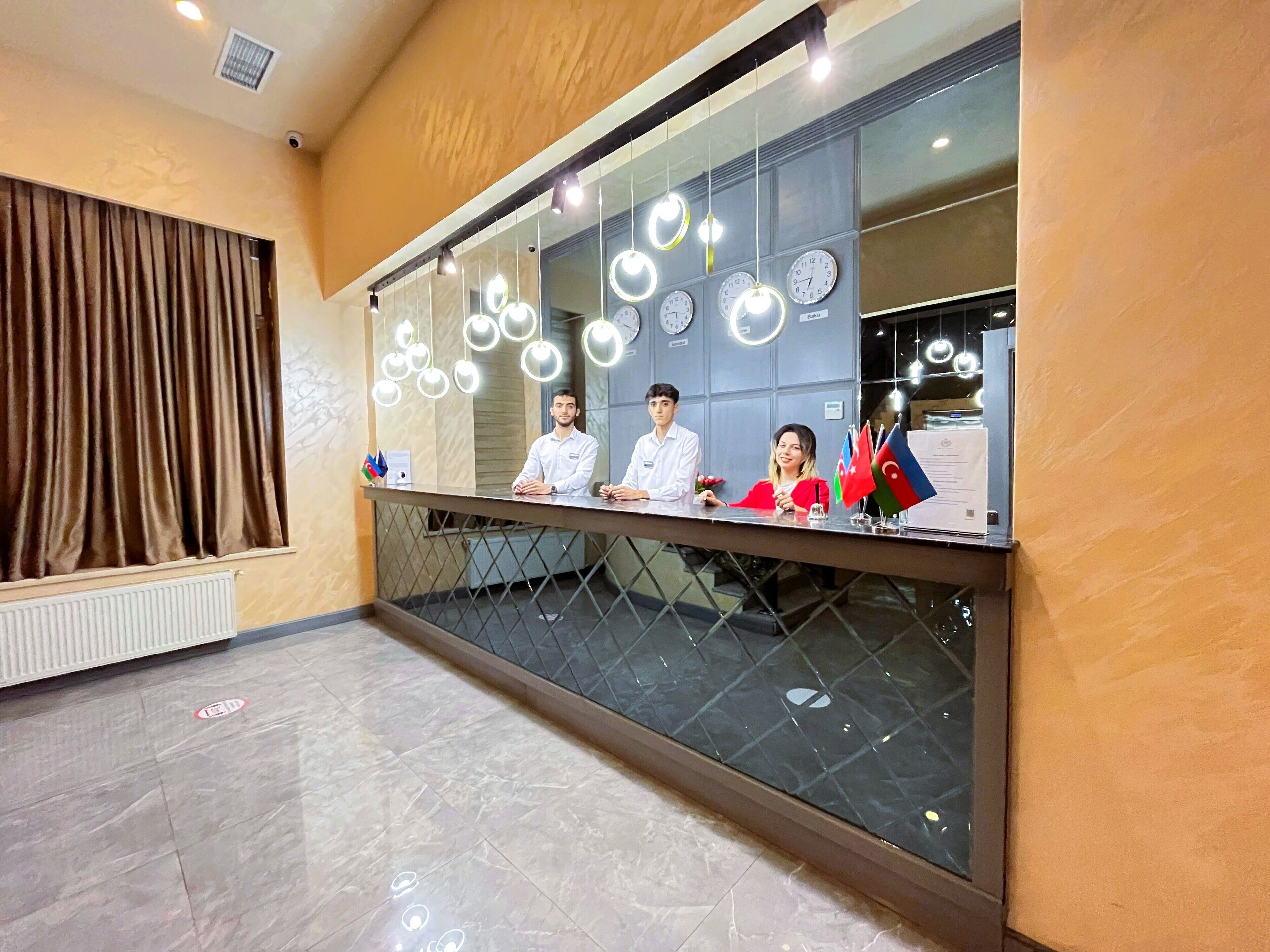 A reception desk with three staff members, a clock, and flags.