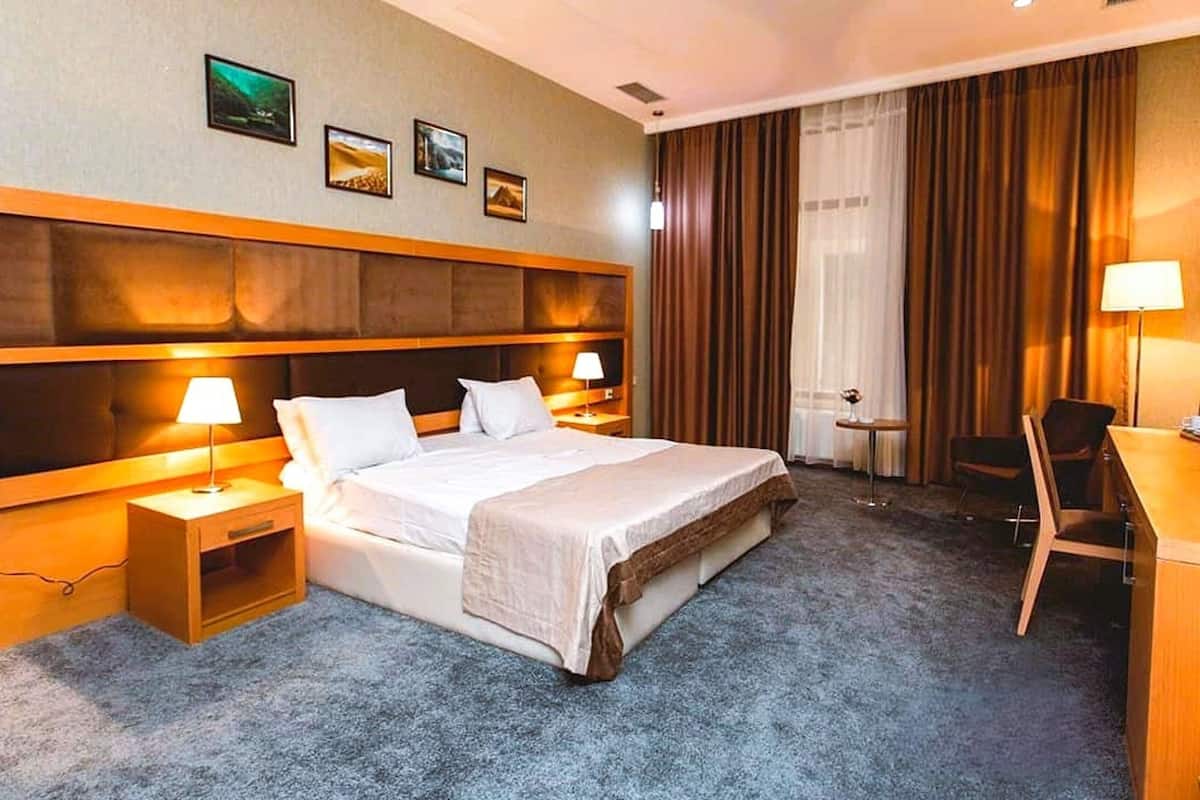 A hotel room with a large bed, two bedside tables with lamps, a desk, and a chair.