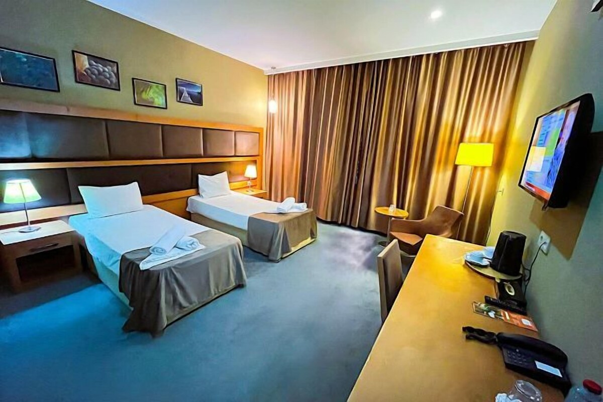 Quarto de hotel com duas camas, uma escrivaninha, uma cadeira, uma televisão e cortina.