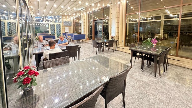 Un comedor interior con mesas y sillas de vidrio, luces colgantes y amplios ventanales.