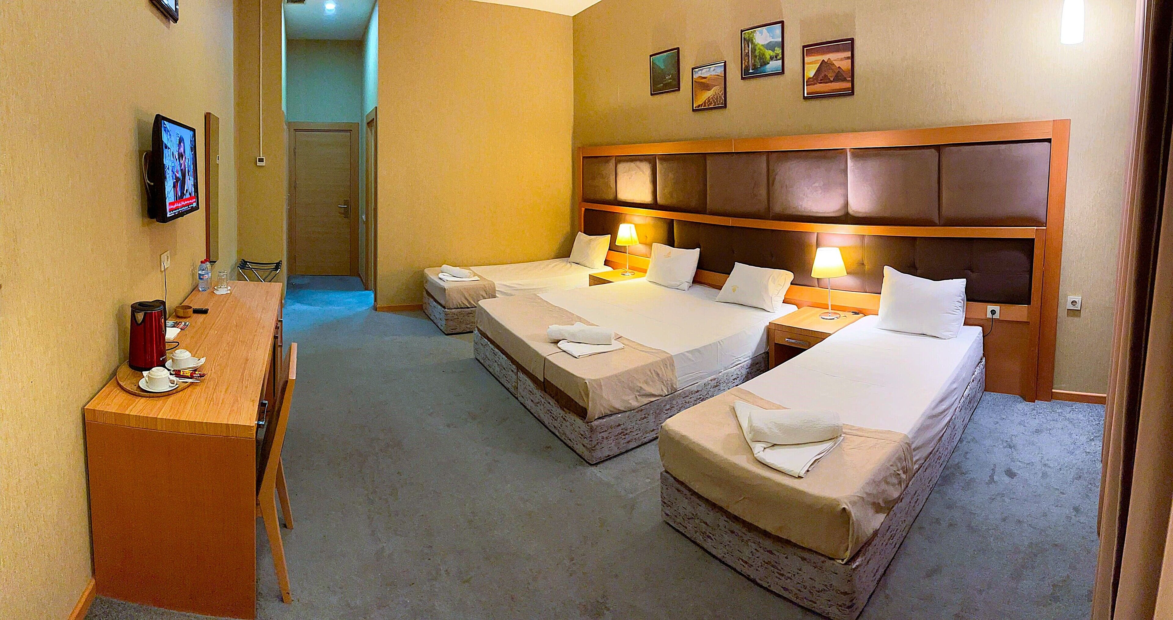 A hotel room with two beds, a desk with a coffee maker, and a TV on the wall.