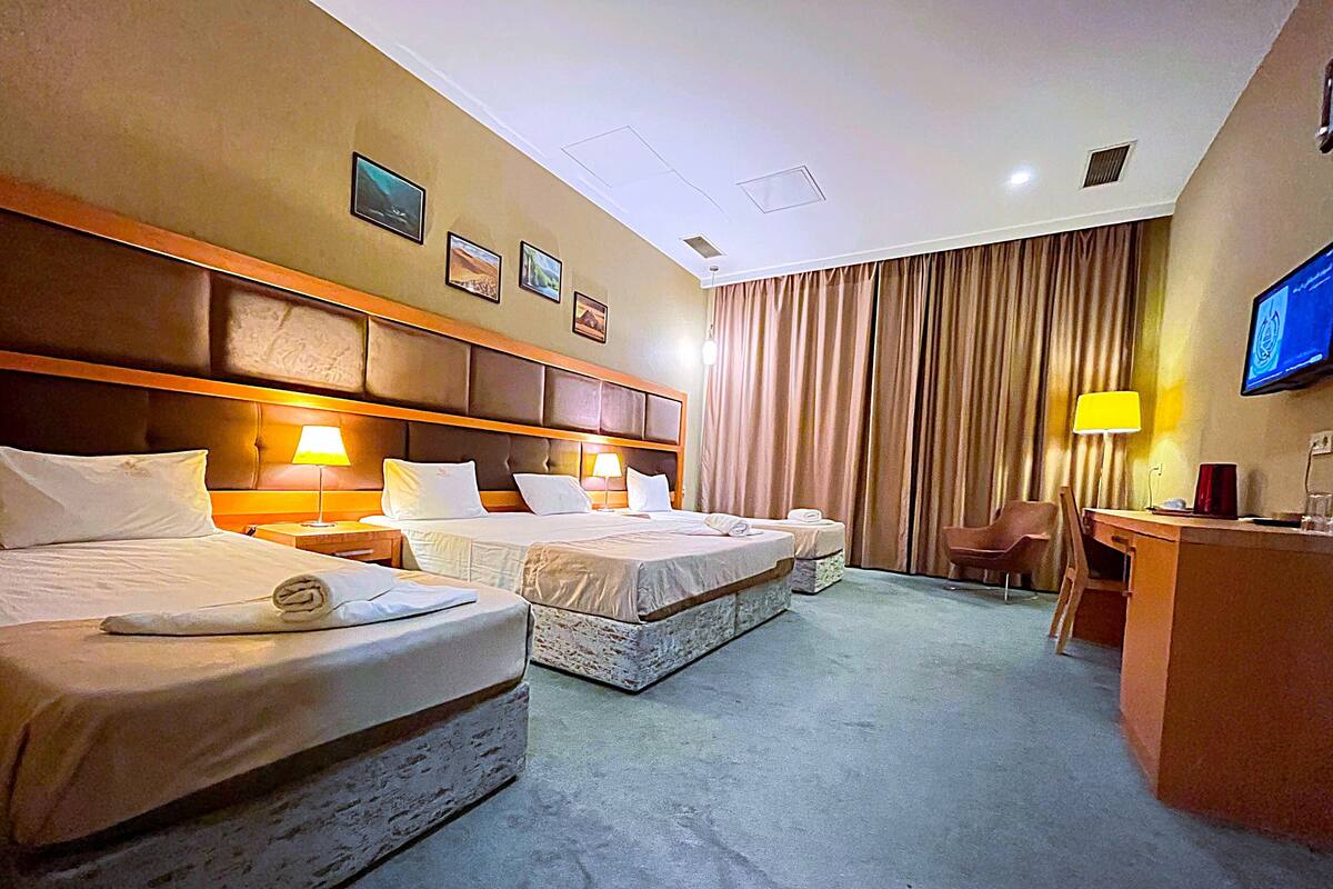 A hotel room with two beds, a desk, a chair, a television, and a large window with curtains.