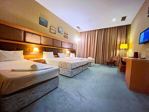 Una habitación de hotel con dos camas, un escritorio, una silla, un televisor y un ventanal con cortinas.