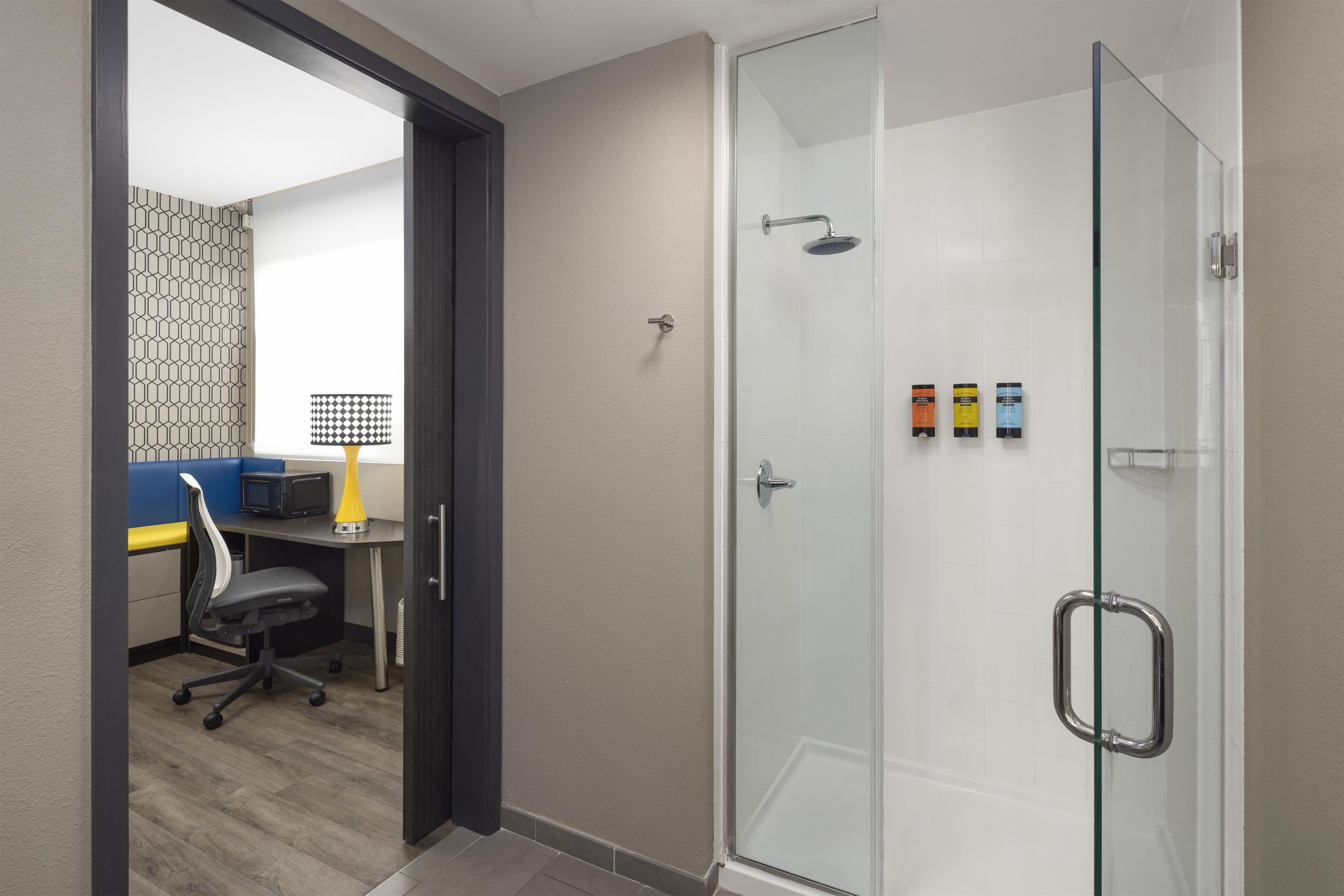 Un baño moderno con cabina de ducha de vidrio, un escritorio con silla y un papel tapiz estampado.