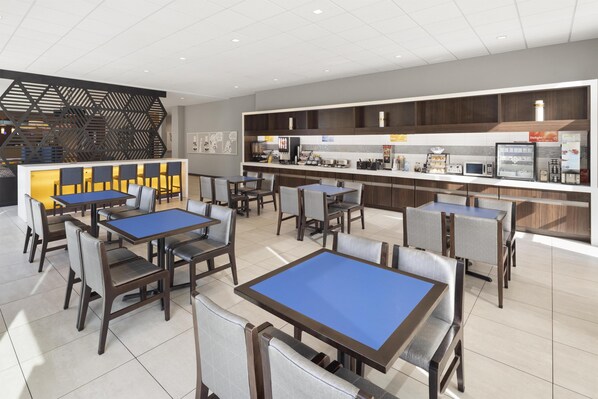 A modern restaurant with blue-topped tables and chairs, a kitchen area with various appliances, and a decorative black partition. - GLō Best Western Nashville Airport (Nashville)