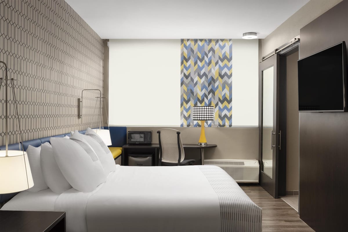 Una camera d'albergo con un letto, un comodino, una lampada, una sedia, una scrivania e un televisore.