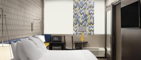 A hotel room with a bed, bedside table, lamp, chair, desk, and a television.