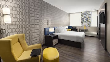 Una habitación de hotel moderna con un muro de patrón geométrico, una cama, un escritorio, una silla y un reposapiés amarillo.