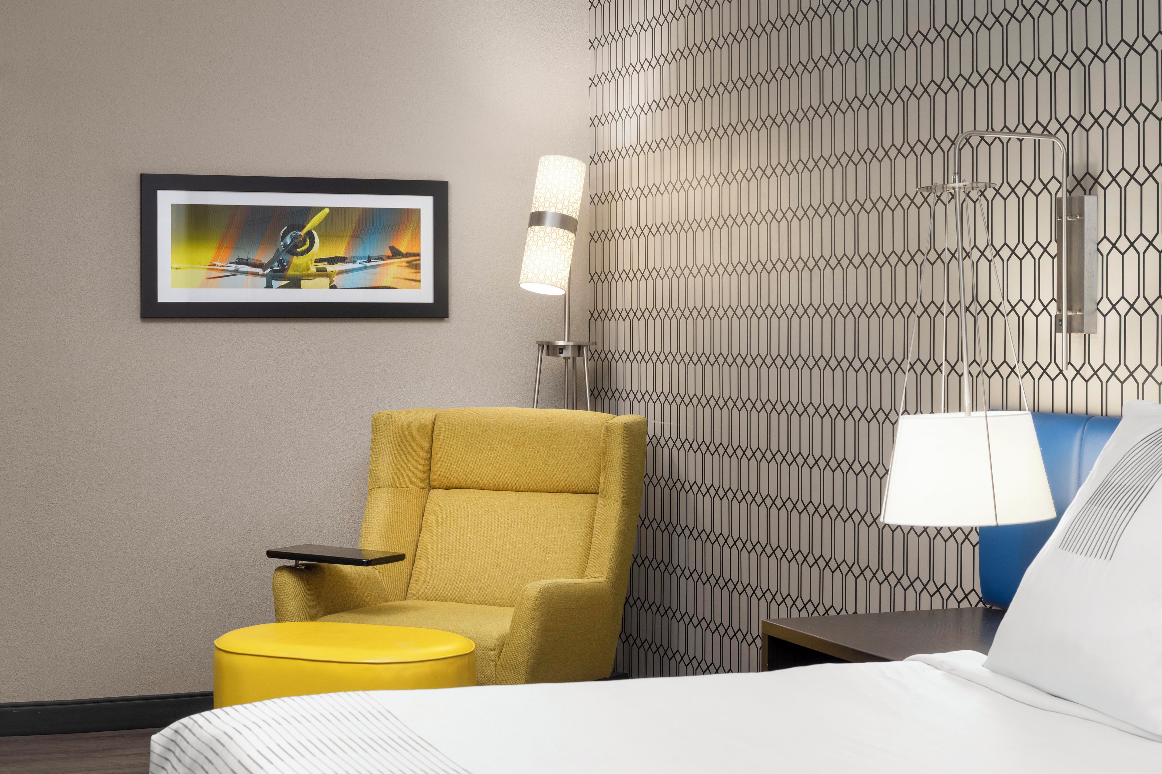 Ein Hotelzimmer mit einem Bett, einem gelben Sessel, einem kleinen Tisch, einer Wandlampe und einem gerahmten Bild.