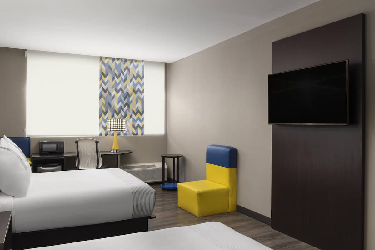 Una camera d'albergo con un letto, una scrivania con un computer, una sedia, una televisione e una finestra con tende a motivi.