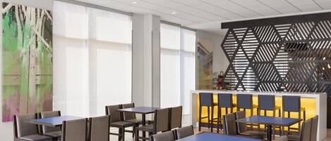 Un intérieur de restaurant moderne, avec de nombreuses tables et chaises, un comptoir doté d’un décor original et de grandes fenêtres laissant entrer la lumière naturelle.