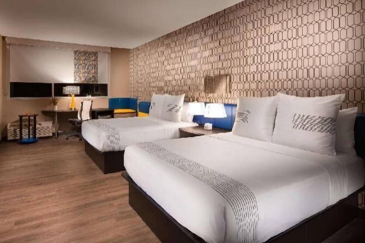 Camera d'albergo con due letti, una scrivania, una sedia, una televisione e una parete decorata.