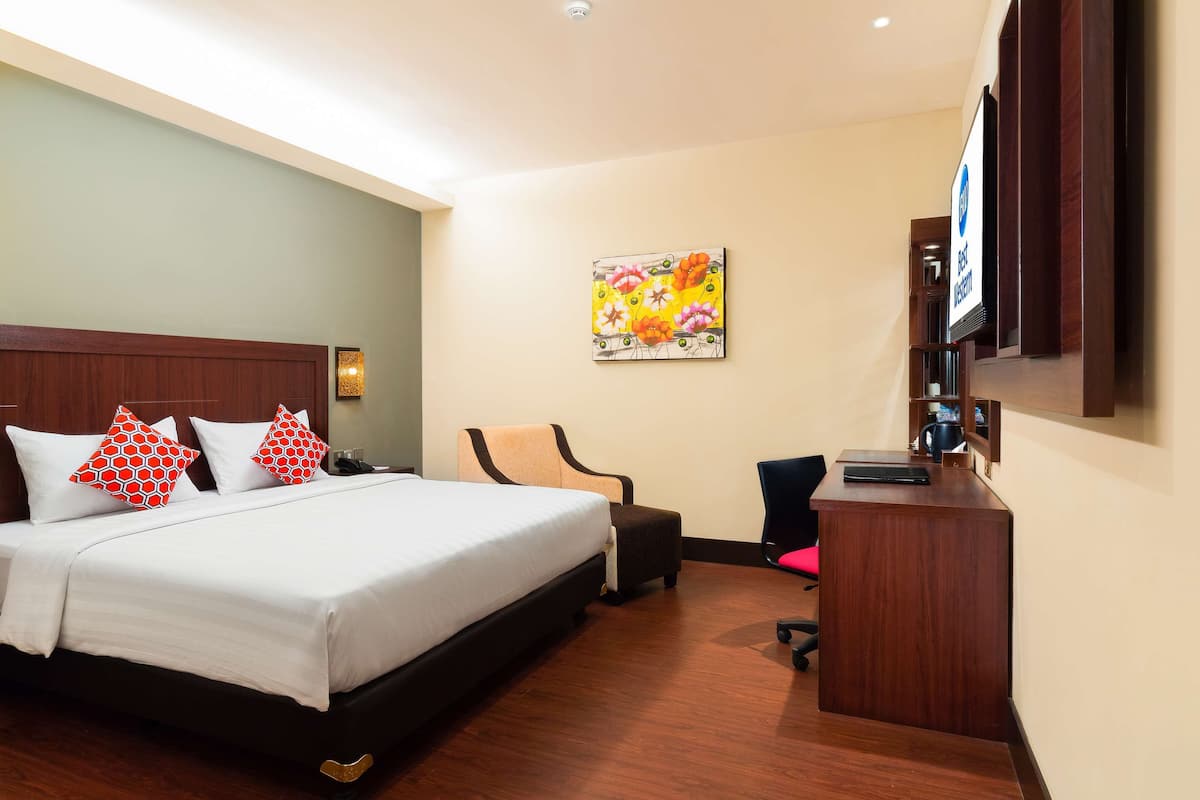 A hotel room with a large bed, a desk, a chair, and a television.