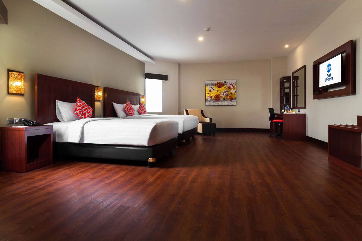 A spacious hotel room with a large bed, two bedside tables, a chair, a desk, and a TV.