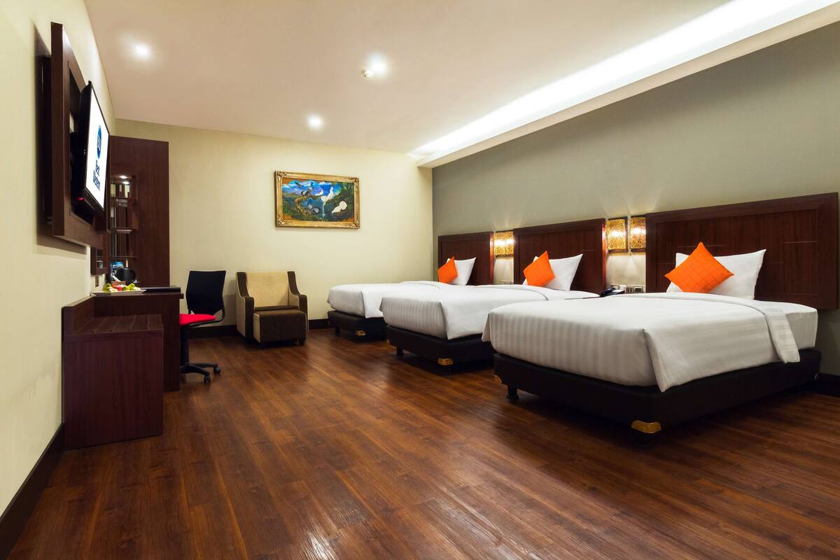 A hotel room with three beds, a desk, a chair, a TV, and a painting on the wall.