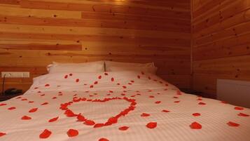Une pièce aux murs lambrissés, avec un lit recouvert de draps blancs et de pétales de roses rouges disposés en forme de cœur.