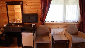 Een gezellige kamer met houten inrichting, een klein bureau met een computer, een televisie, twee fauteuils en een raam met gordijnen.