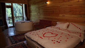 A wooden cabin bedroom with a large bed, a chair, a bathtub, and a view of the forest. - Abant Kartal Yuvasi Hotel (Bolu)