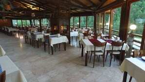 A spacious dining area with tables and chairs, large windows, and a stone fireplace. - Abant Kartal Yuvasi Hotel (Bolu)