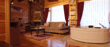 Una cabaña acogedora de madera con chimenea de piedra, un sofá, una mesa de centro y una bañera.
